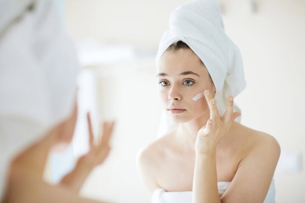 Woman in a towel moisturizing her face after a shower to slow spray tan fading